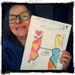 Die Autorin Sandra Baumgärtner hält ein Blatt in die Höhe, auf dem der Buchstabe H und ein handgeschriebenes ABC zu sehen ist